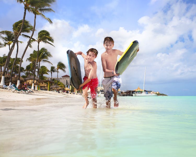 Two children with kneeboards running along beach.