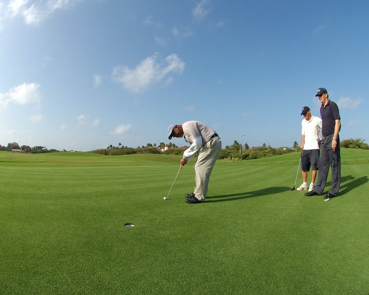 Man putting on golf green as others watch on.